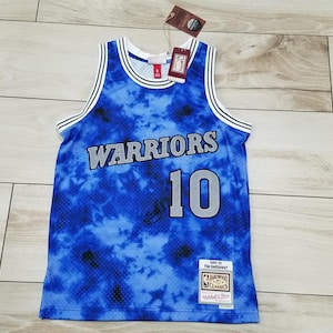 May include: A blue tie-dye Warriors basketball jersey with the number 10 in gray. The jersey has white and black trim around the neck and armholes. The word "Warriors" is across the chest in gray.