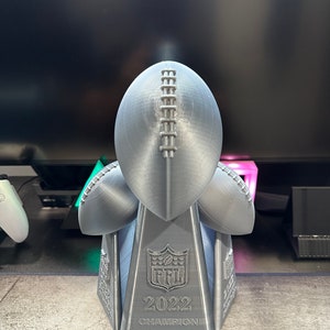Op de afbeelding: Een zilveren 3D-geprinte trofee in de vorm van een voetbal met de tekst "2022 Champion Worst League Ever" op de basis.