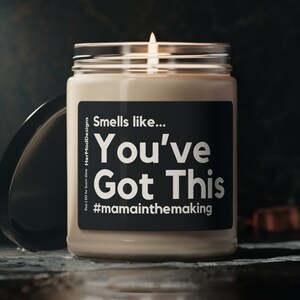 Puede incluir: Una vela beige con una etiqueta negra que dice "Smells like... You've Got This #mamainthemaking". La vela está encendida y la llama es visible.
