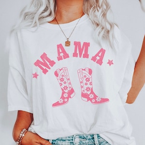 May include: White t-shirt with pink text that says "MAMA" and a pair of pink cowboy boots with floral designs.