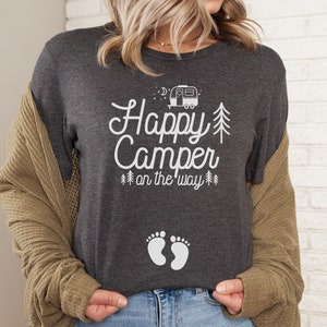 May include: A dark gray t-shirt with the text "Happy Camper on the way" and a small camper icon. There are also two white footprints on the shirt.