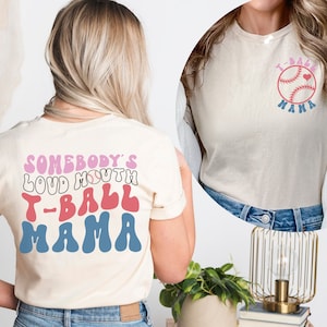 May include: Two white t-shirts with a baseball theme. The front of the shirt says "T-Ball Mama" with a baseball and heart. The back of the shirt says "Somebody's Loud Mouth T-Ball Mama" in a retro font.