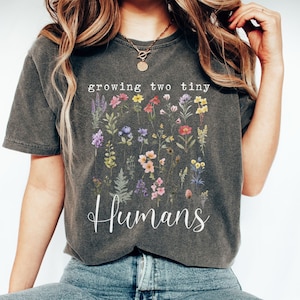 May include: A gray t-shirt with a floral design and the text "growing two tiny humans".