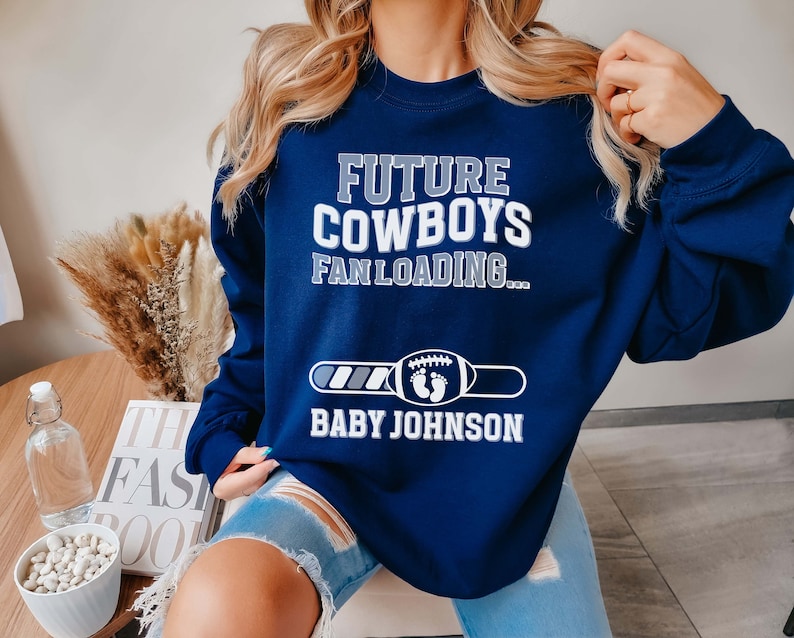 Puede incluir: Sudadera azul marino con el texto "Future Cowboys Fan Loading..." y una barra de progreso con el texto "Baby Johnson".