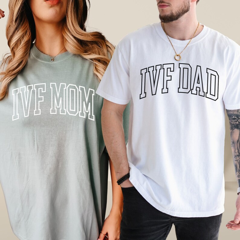 May include: A couple wearing matching t-shirts. The woman's shirt is light green with the text "IVF MOM" in white. The man's shirt is white with the text "IVF DAD" in black.