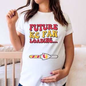 May include: White t-shirt with the text "FUTURE KC FAN LOADING..." in red and yellow letters. A progress bar with a red and yellow arrowhead and two footprints is below the text.