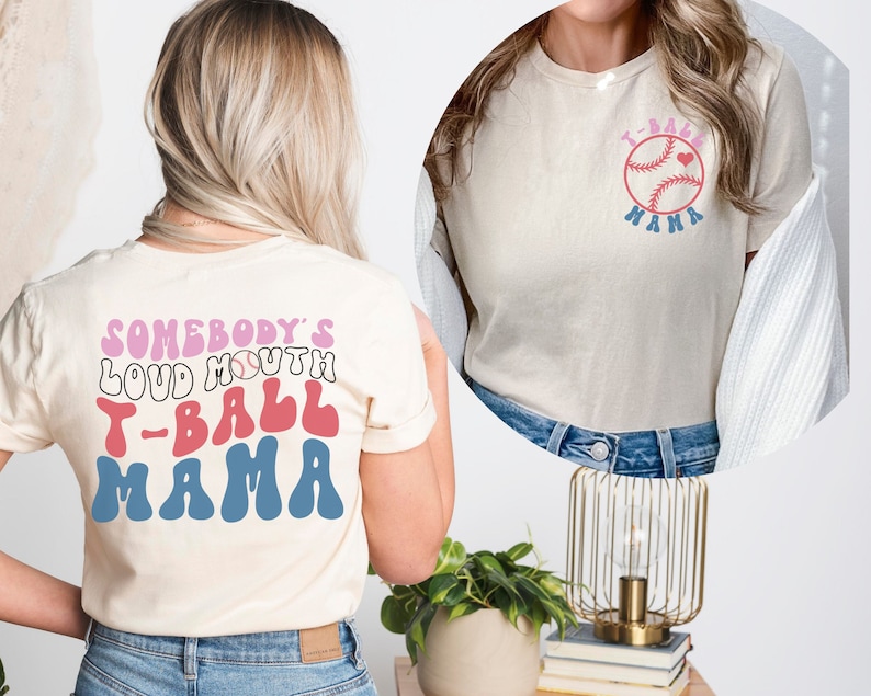 May include: Two white t-shirts with a baseball theme. The front of the shirt says "T-Ball Mama" with a baseball and heart. The back of the shirt says "Somebody's Loud Mouth T-Ball Mama" in a retro font.
