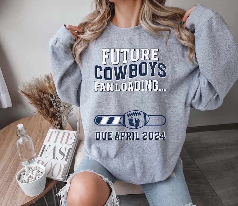 Puede incluir: Sudadera gris con el texto "Future Cowboys Fan Loading..." y una barra de progreso con un bal&oacute;n de f&uacute;tbol y huellas de pies de beb&eacute;. La barra de progreso indica "Due April 2024".