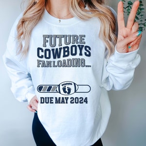 Puede incluir: Sudadera blanca con el texto "Future Cowboys Fan Loading..." y una barra de progreso con un bal&oacute;n de f&uacute;tbol y huellas de pies de beb&eacute;. La barra de progreso indica "Due May 2024".