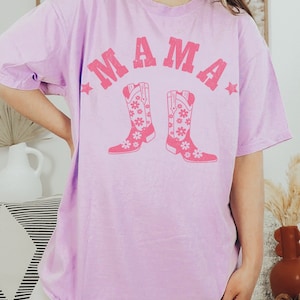 May include: A lavender t-shirt with the word "MAMA" in pink letters and a pair of pink cowboy boots with floral designs.