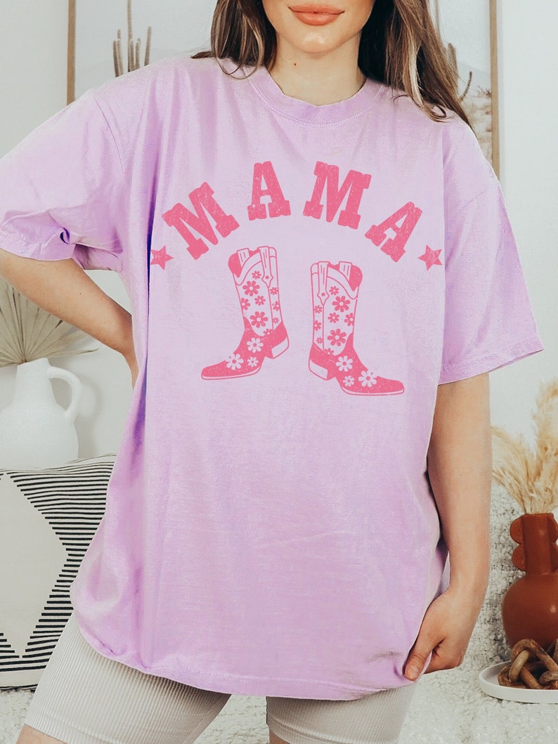 May include: A lavender t-shirt with the word "MAMA" in pink letters and a pair of pink cowboy boots with floral designs.