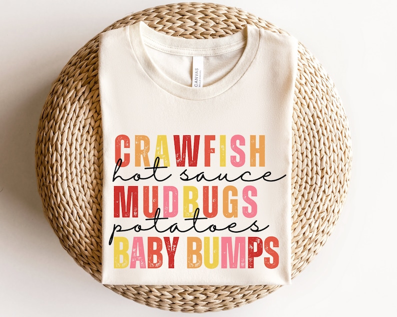 Puede incluir: Una camiseta blanca con un dise&ntilde;o gr&aacute;fico colorido que dice "Crawfish hot sauce Mudbugs potatoes Baby bumps".