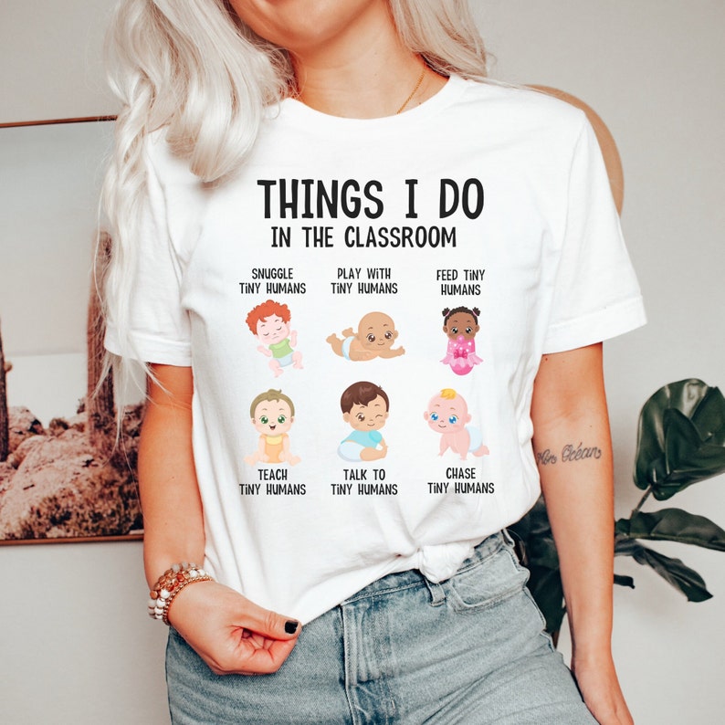 May include: White t-shirt with the text "THINGS I DO IN THE CLASSROOM" and illustrations of babies with text describing activities like "SNUGGLE TINY HUMANS", "PLAY WITH TINY HUMANS", "FEED TINY HUMANS", "TEACH TINY HUMANS", "TALK TO TINY HUMANS", and "CHASE TINY HUMANS".