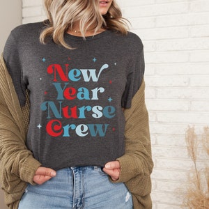 May include: A dark grey t-shirt with the text "New Year Nurse Crew" in blue and red lettering with white stars.