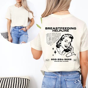 May include: A white t-shirt with a black graphic of a woman on the phone with the text "Breastfeeding Helpline I'm Here To Help 800-994-9662 You're Not Alone! 24/7 365"