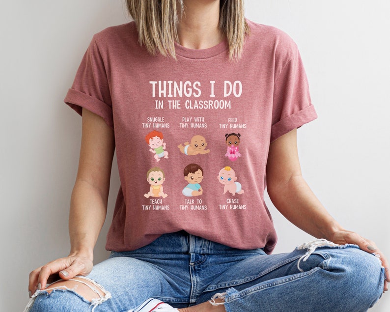May include: A pink t-shirt with the text "Things I do in the classroom" and illustrations of babies. The text below the illustrations includes phrases like "Snuggle tiny humans", "Play with tiny humans", "Feed tiny humans", "Teach tiny humans", "Talk to tiny humans", and "Chase tiny humans".