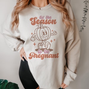 May include: A light grey sweatshirt with a retro-style graphic of a pumpkin walking and the text "'tis the season to be pregnant".