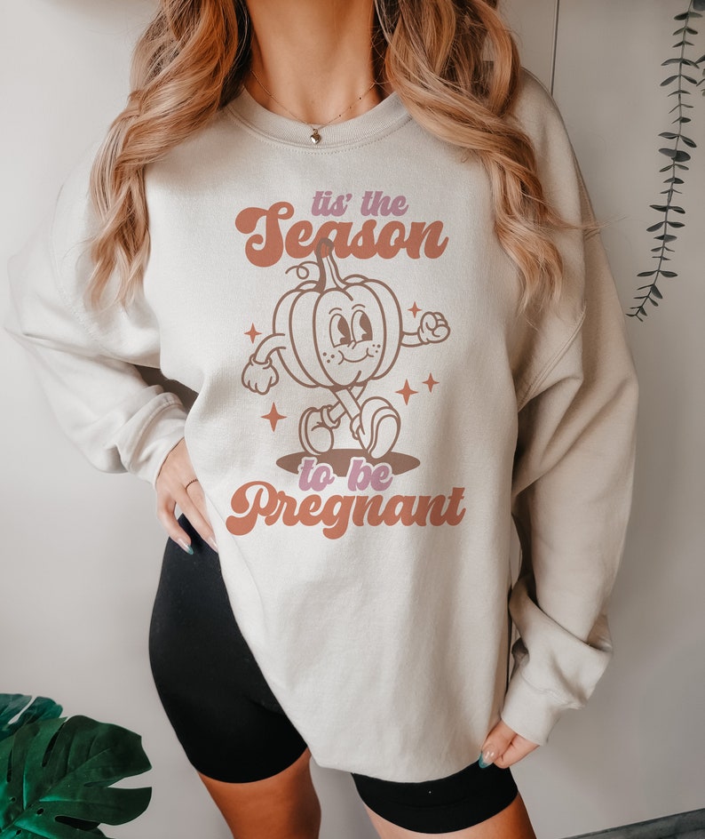 May include: A light grey sweatshirt with a retro-style graphic of a pumpkin walking and the text "'tis the season to be pregnant".