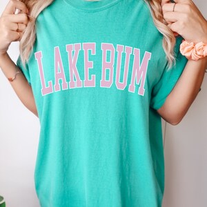 May include: A turquoise blue t-shirt with a pink graphic that says "LAKE BUM" in a collegiate font.
