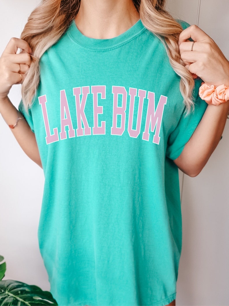 May include: A turquoise blue t-shirt with a pink graphic that says "LAKE BUM" in a collegiate font.
