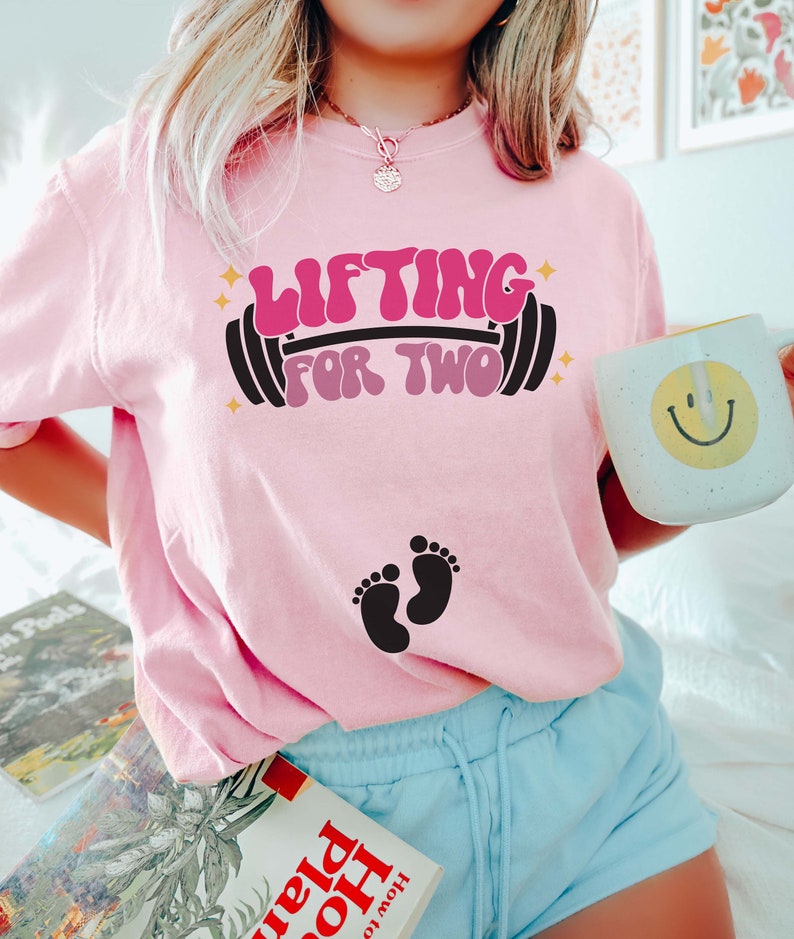 May include: Pink t-shirt with the text "Lifting for Two" in a retro font with a barbell and two baby footprints.