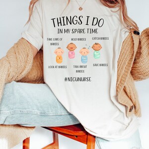 May include: A white t-shirt with the text "THINGS I DO IN MY SPARE TIME" and a series of illustrations of babies with the text "TAKE CARE OF BABIES", "HOLD BABIES", "CATCH BABIES", "LOOK AT BABIES", "TALK ABOUT BABIES", "SAVE BABIES" and the hashtag "#NICUNURSE".