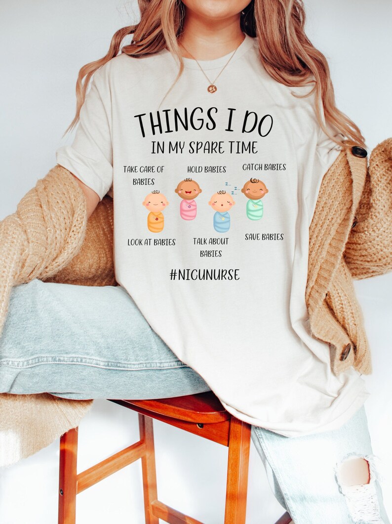 May include: A white t-shirt with the text "THINGS I DO IN MY SPARE TIME" and a series of illustrations of babies with the text "TAKE CARE OF BABIES", "HOLD BABIES", "CATCH BABIES", "LOOK AT BABIES", "TALK ABOUT BABIES", "SAVE BABIES" and the hashtag "#NICUNURSE".