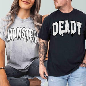 May include: Two t-shirts with a Halloween theme. The white t-shirt has the text "MOMSTER" in black with dripping paint. The black t-shirt has the text "DEADLY" in white with dripping paint.