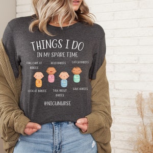 May include: A dark gray t-shirt with the text "THINGS I DO IN MY SPARE TIME" and a graphic of five cartoon babies in swaddles. The text below the graphic reads "TAKE CARE OF BABIES, HOLD BABIES, CATCH BABIES, LOOK AT BABIES, TALK ABOUT BABIES, SAVE BABIES" and "#NICUNURSE".
