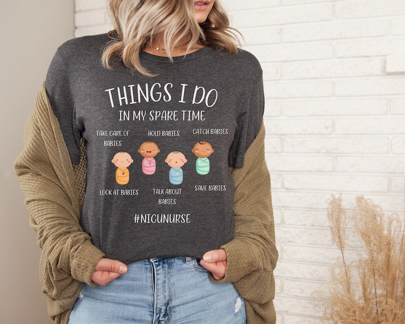 May include: A dark gray t-shirt with the text "THINGS I DO IN MY SPARE TIME" and a graphic of five cartoon babies in swaddles. The text below the graphic reads "TAKE CARE OF BABIES, HOLD BABIES, CATCH BABIES, LOOK AT BABIES, TALK ABOUT BABIES, SAVE BABIES" and "#NICUNURSE".