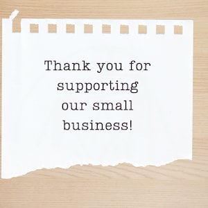 May include: A white piece of paper with a torn edge, on a wood background. The paper has the text "Thank you for supporting our small business!" written on it.