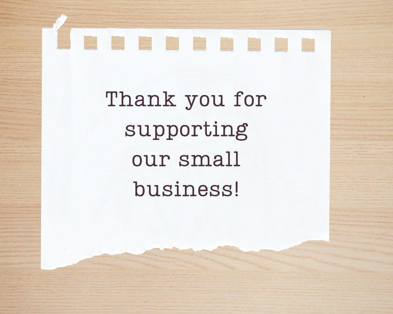 May include: A white piece of paper with a torn edge, on a wood background. The paper has the text "Thank you for supporting our small business!" written on it.