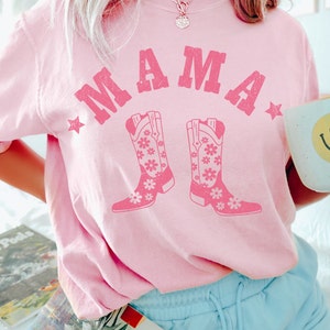 May include: Pink t-shirt with the text "MAMA" in a vintage style font with two pink cowboy boots with floral designs.