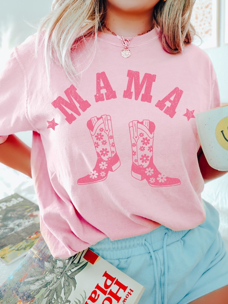 May include: Pink t-shirt with the text "MAMA" in a vintage style font with two pink cowboy boots with floral designs.