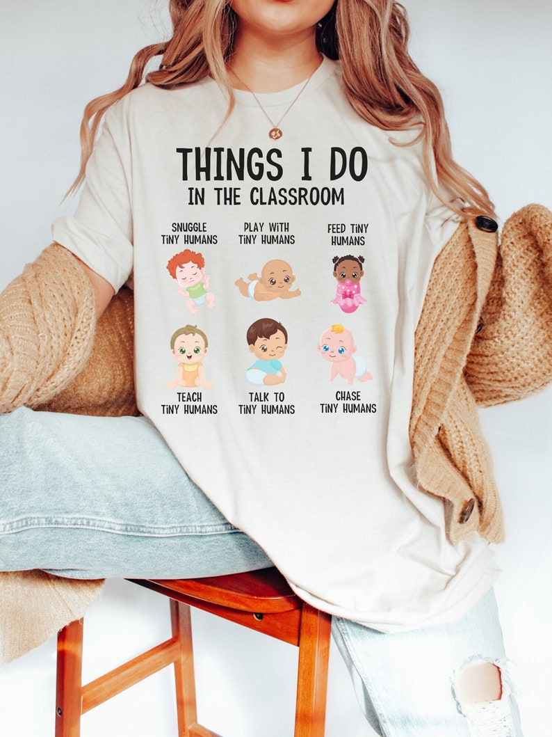 May include: A white t-shirt with the text "Things I do in the classroom" and illustrations of babies with text describing activities like "Snuggle Tiny Humans", "Play with Tiny Humans", "Feed Tiny Humans", "Teach Tiny Humans", "Talk to Tiny Humans", and "Chase Tiny Humans".