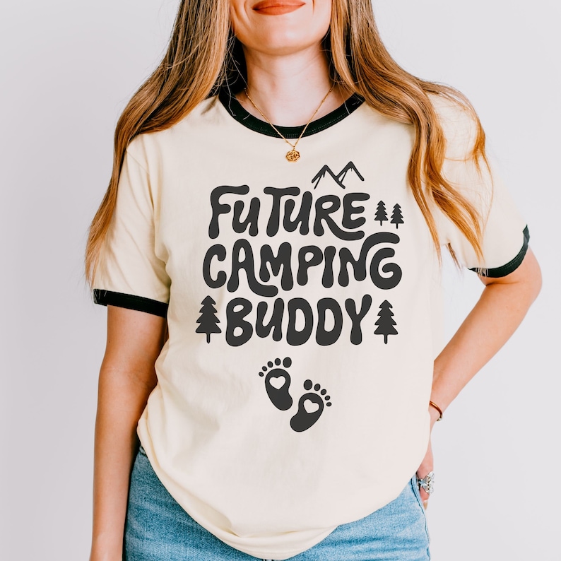 Może przedstawiać: Jasnoż&oacute;łta koszulka z czarnym kołnierzem. Koszulka ma czarny nadruk z napisem "Future Camping Buddy" i parą ślad&oacute;w st&oacute;p pod tekstem.
