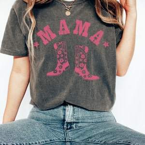 May include: A gray t-shirt with a pink graphic of the word "MAMA" with two pink cowboy boots with floral designs on them.