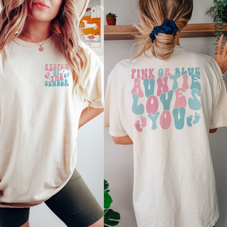 Puede incluir: Dos mujeres con camisetas de color beige claro con diferentes textos impresos en la espalda. La camiseta de la izquierda dice "Keeper of the Gender" con un dise&ntilde;o de huella de pie azul y rosa. La camiseta de la derecha dice "Pink or Blue Auntie Loves You" con un coraz&oacute;n rosa y huellas de pie azul y rosa.