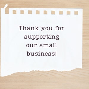 May include: A white piece of paper with a torn edge, on a wood background. The paper has the text "Thank you for supporting our small business!" written on it.