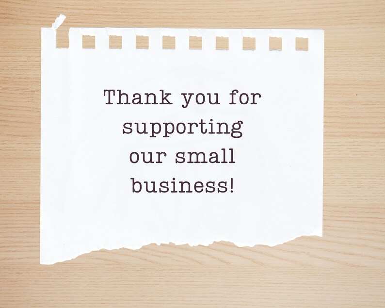 May include: A white piece of paper with a torn edge, on a wood background. The paper has the text "Thank you for supporting our small business!" written on it.