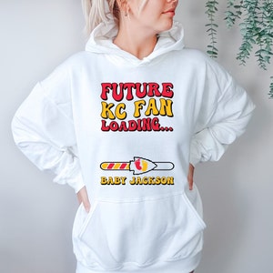 May include: White hoodie with a red and yellow graphic that says "Future KC Fan Loading..." with a progress bar and the text "Baby Jackson".
