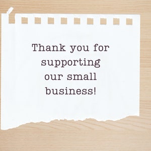 May include: A white piece of paper with a torn edge, on a wood background. The paper has the text "Thank you for supporting our small business!" written on it.