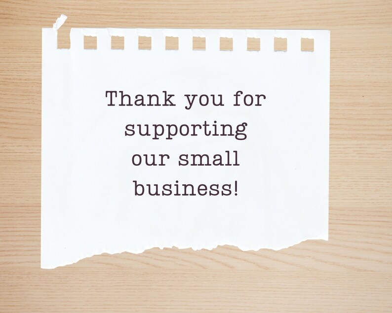May include: A white piece of paper with a torn edge, on a wood background. The paper has the text "Thank you for supporting our small business!" written on it.