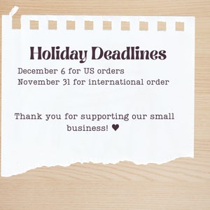 May include: A white piece of paper with a torn edge, with the text "Holiday Deadlines" in black. The text below reads "December 6 for US orders" and "November 31 for international order". The text at the bottom reads "Thank you for supporting our small business!" with a black heart symbol.