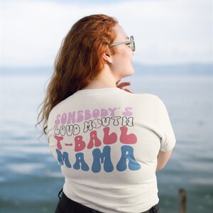 May include: White t-shirt with a pink, blue, and white graphic that says "Somebody's Loud Mouth T-Ball Mama".
