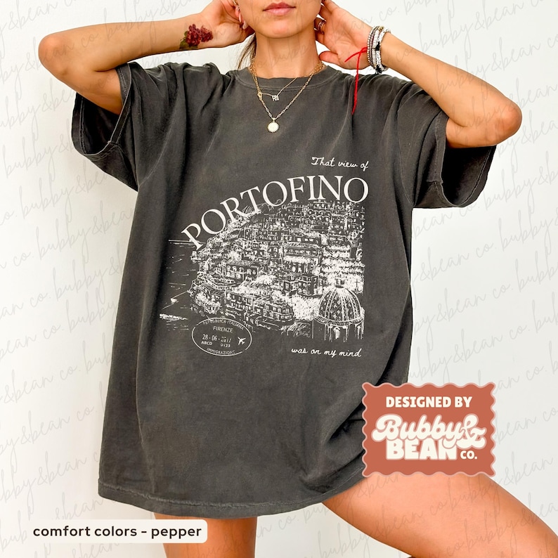 May include: Dark gray t-shirt with a white graphic of the town of Portofino, Italy, and the text "That view of PORTOFINO was on my mind." The shirt also has the text "Designed by Bubby & Bean Co."