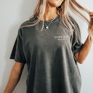 May include: A dark gray oversized t-shirt with the text "DOWN BAD - Fitness Club" printed on the front.