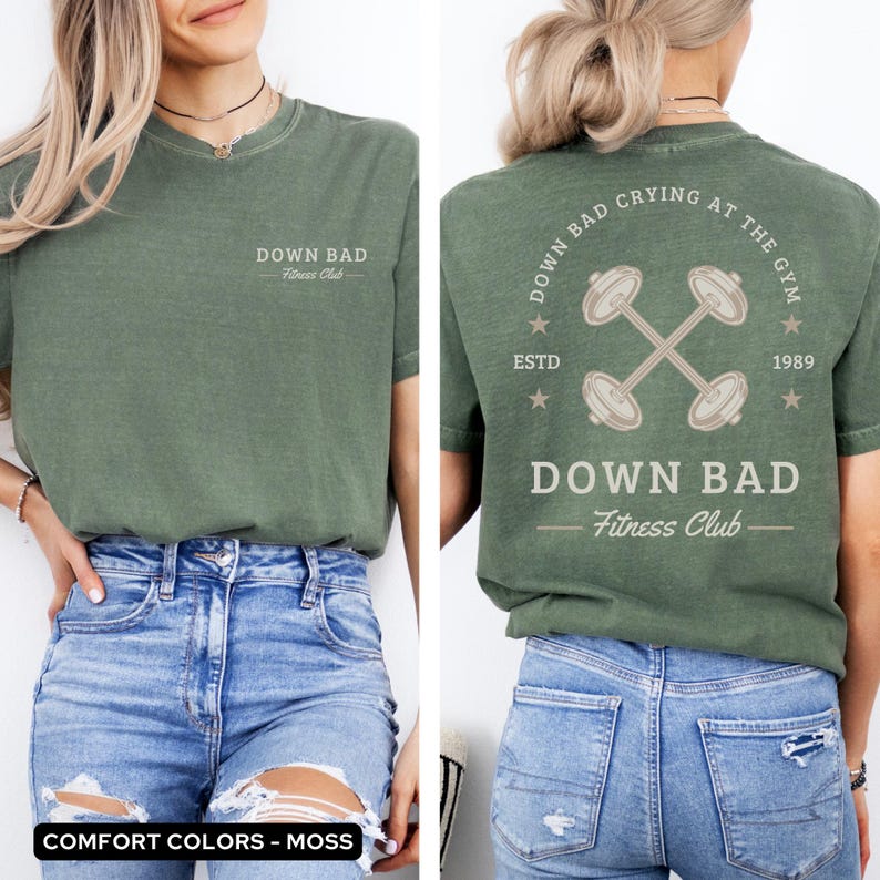 May include: A green t-shirt with a distressed look featuring the text "Down Bad Fitness Club" on the front and the text "Down Bad Crying At The Gym Estd 1989" with a crossed dumbbell graphic on the back.