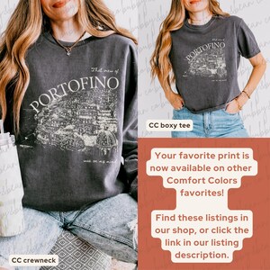 May include: Dark gray crewneck sweatshirt and t-shirt featuring a graphic of Portofino, Italy, with the text "That view of Portofino was on my mind." The t-shirt is a boxy style. The image also includes text about the print being available on other Comfort Colors favorites.