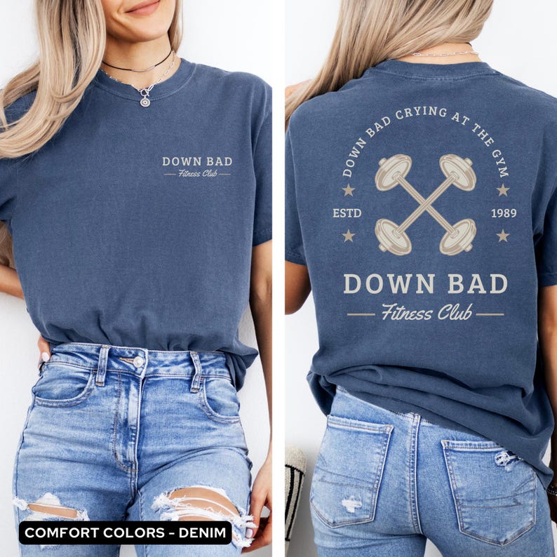 May include: A blue t-shirt with a white graphic design on the front and back. The front design says "Down Bad - Fitness Club". The back design says "Down Bad - Fitness Club" with a crossed dumbbell graphic and the text "Down Bad Crying At The Gym - Estd 1989".